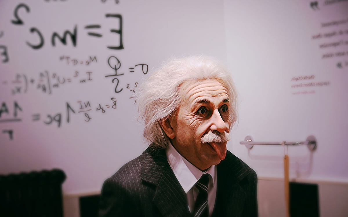 Lifelike wax figure of Albert Einstein sticking out his tongue in front of a chalkboard filled with physics equations