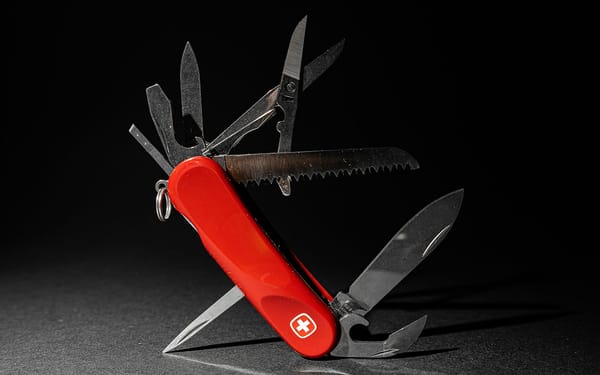 Close-up of a classic red Swiss Army knife multi-tool with built-in flashlight and folded silver implements, on a light neutral background with sharp metallic details.